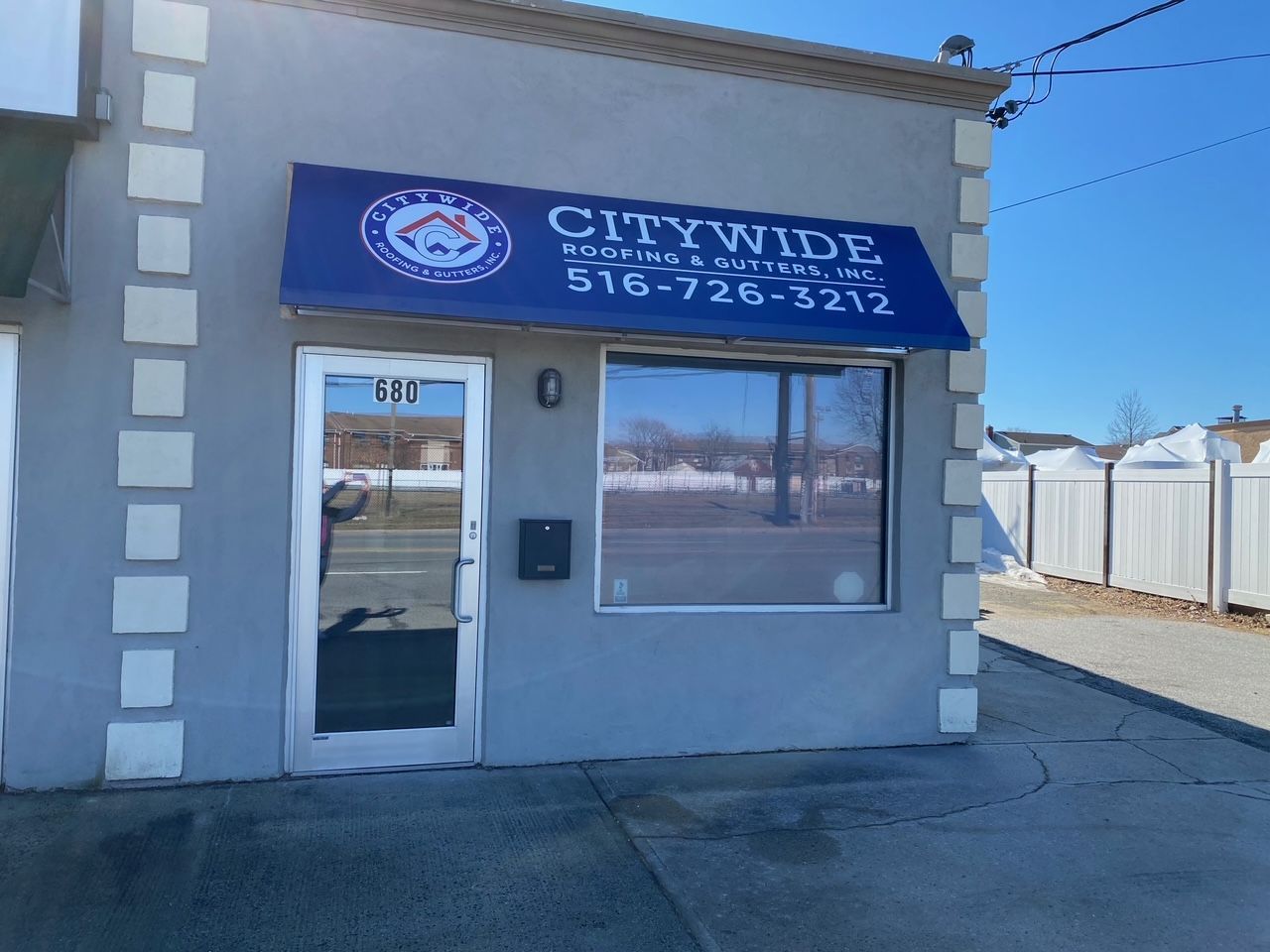 Small grey storefront with a blue awning displaying the business name 