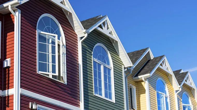A row of colorful, multi-story townhomes with arched windows and shingled siding under a clear blue sky.