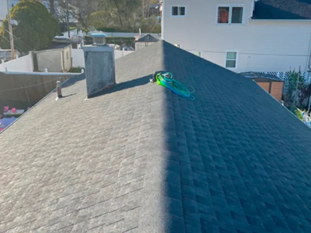 A dark grey shingled roof with a chimney and a coiled green garden hose resting on the ridge.