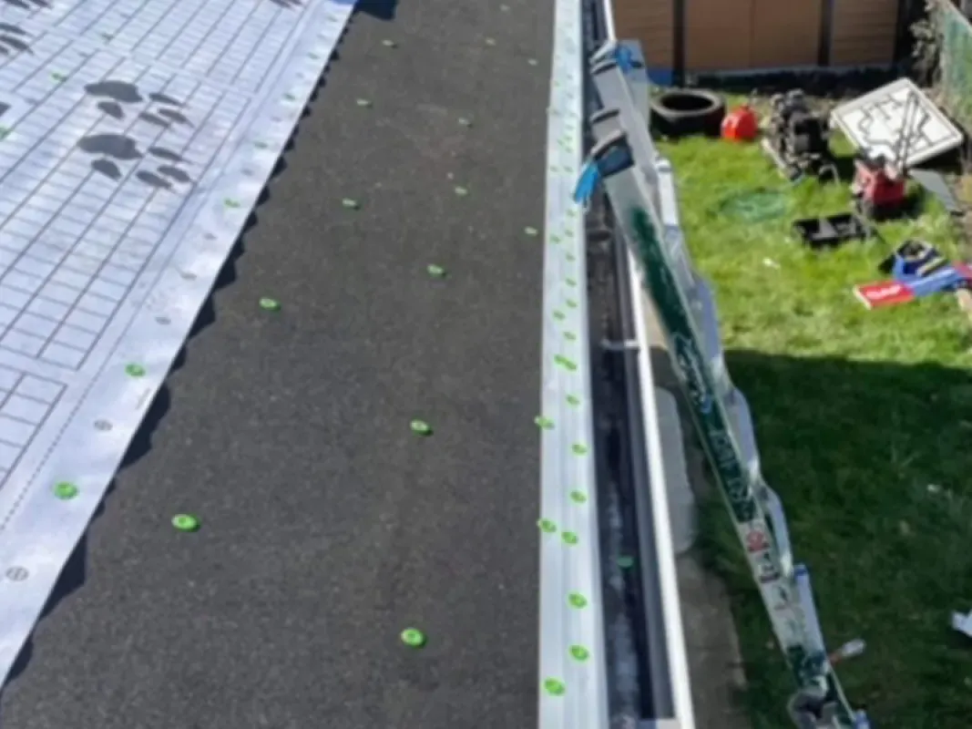 A view from above showing a roof under repair with protective underlayment installed and a ladder leaning against the side.
