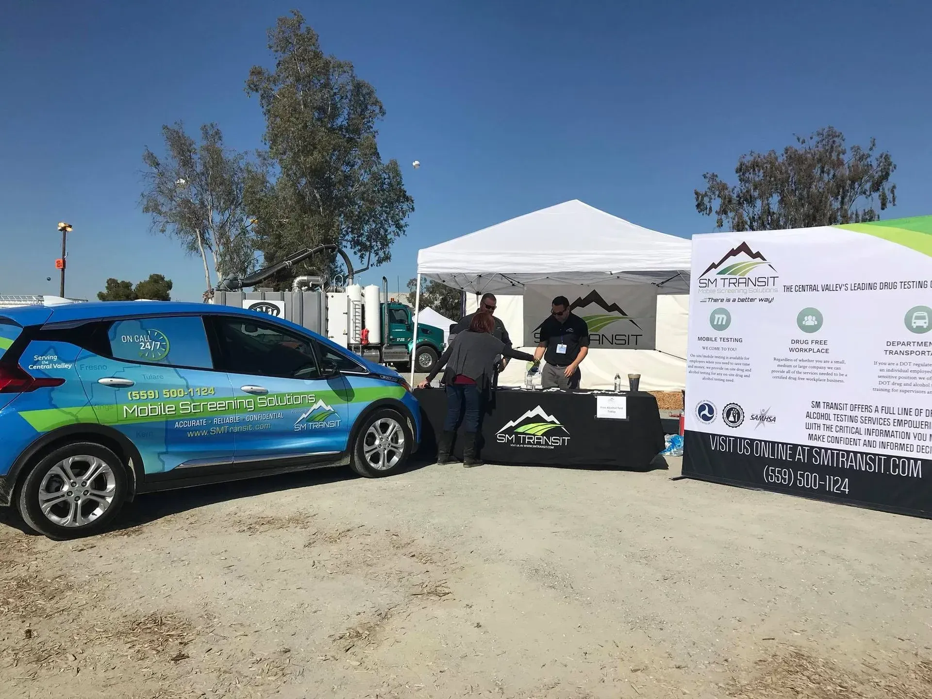A blue car is parked in a parking lot next to a tent.