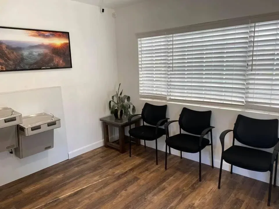 A waiting room with black chairs and a picture on the wall.
