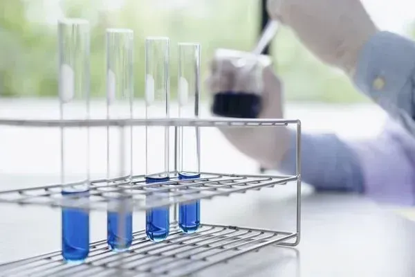 A person is pouring blue liquid into test tubes.