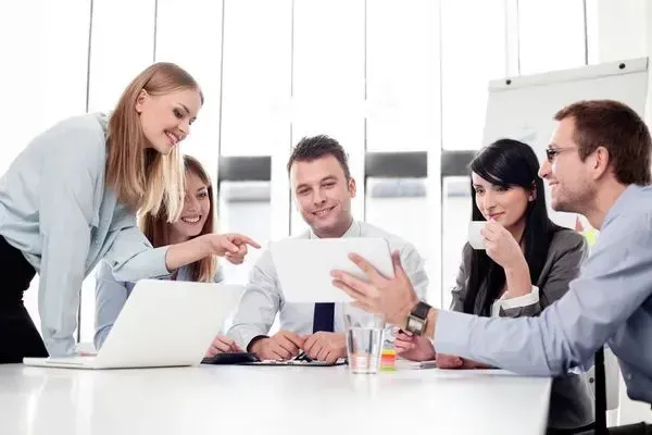 A group of people are sitting around a table looking at a laptop.