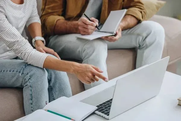A man and a woman are sitting on a couch looking at a laptop.