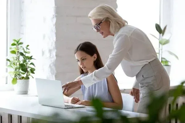 A woman is teaching another woman how to use a laptop computer.
