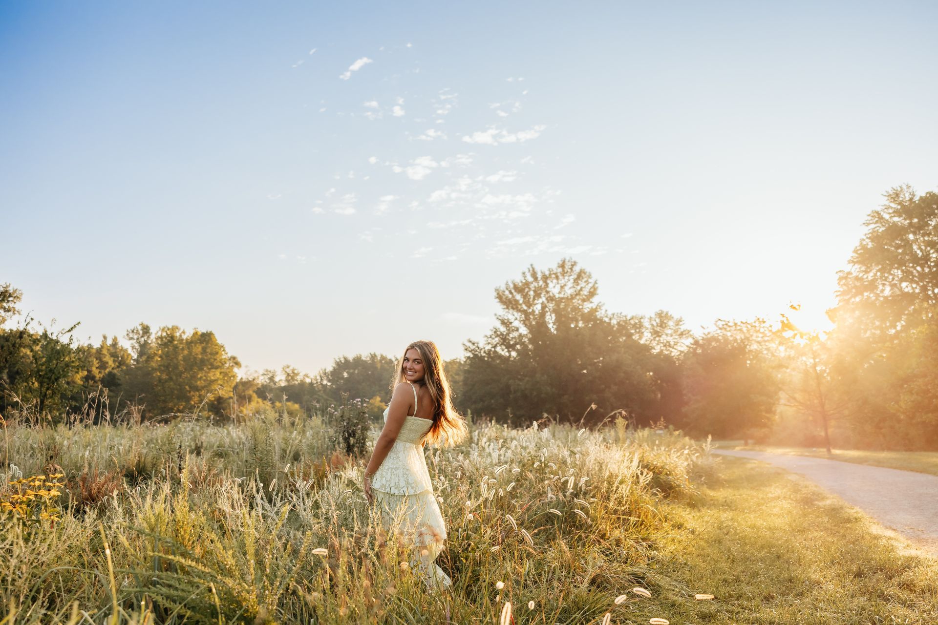 Woman in white dress smiles, stands in sunlit field.