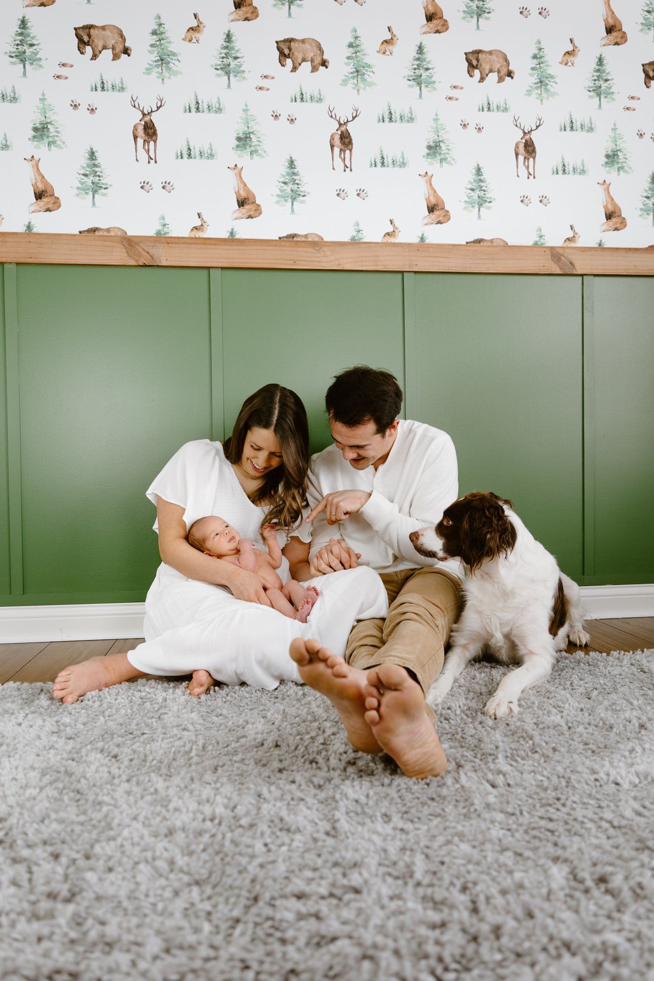 Mom and dad sit in the nursery with their baby and dog