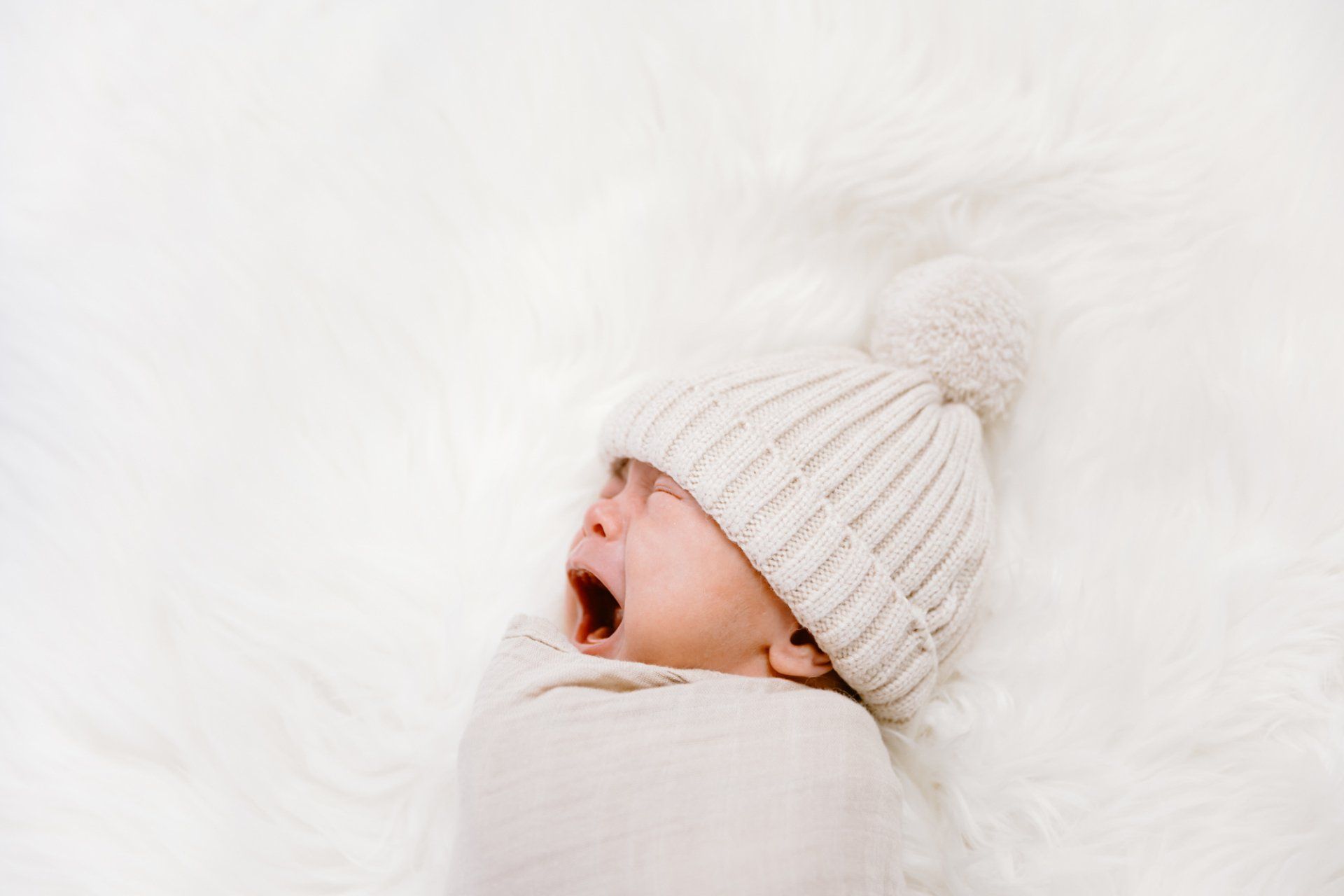 Newborn baby boy cries while wearing a hat