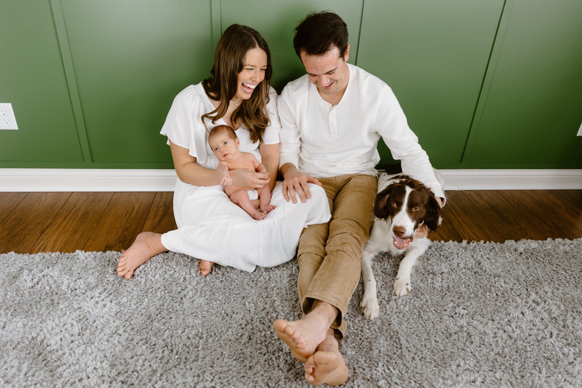 Mom and dad sit on the ground with their baby and dog