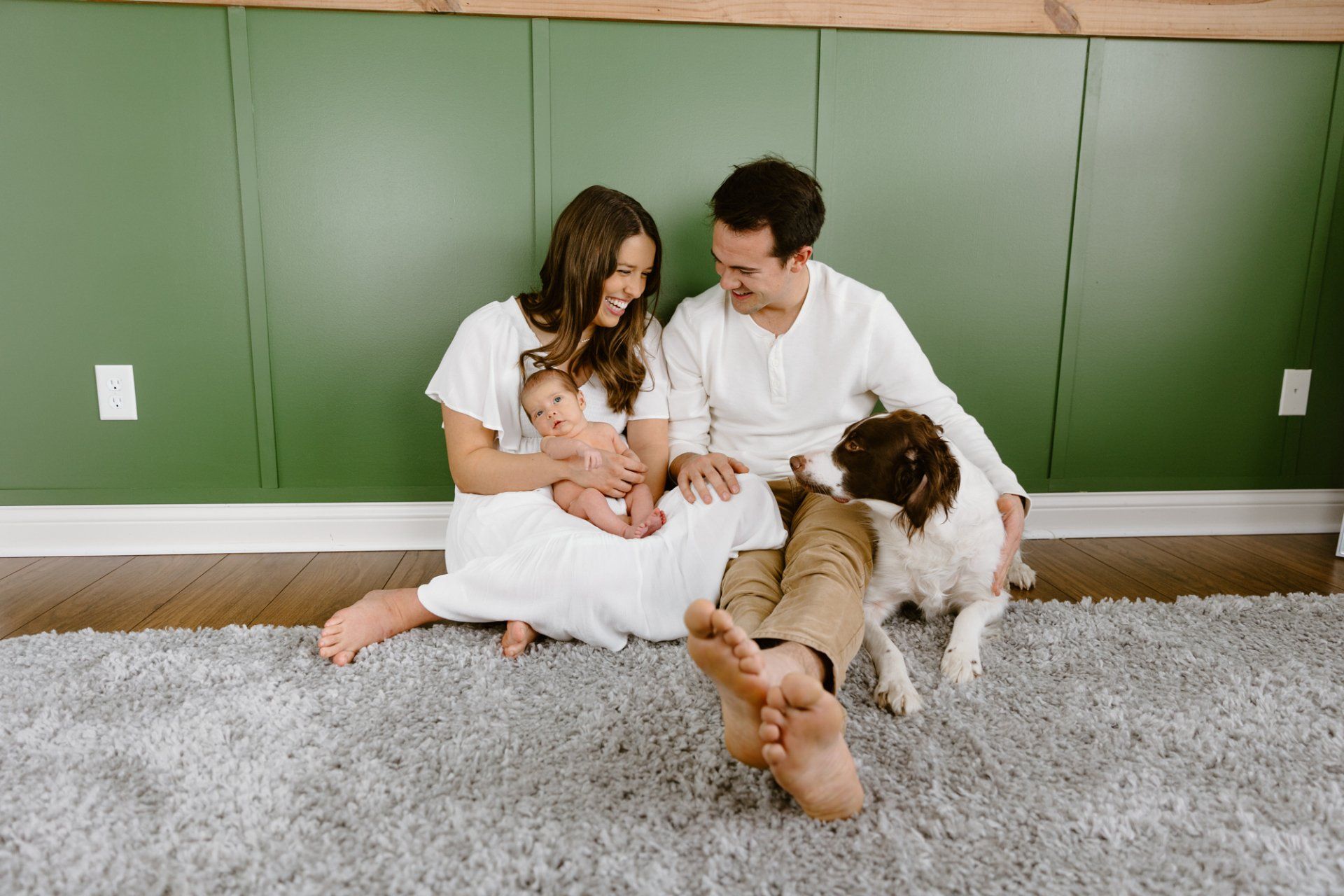 Mom and dad sit on the ground with baby and dog