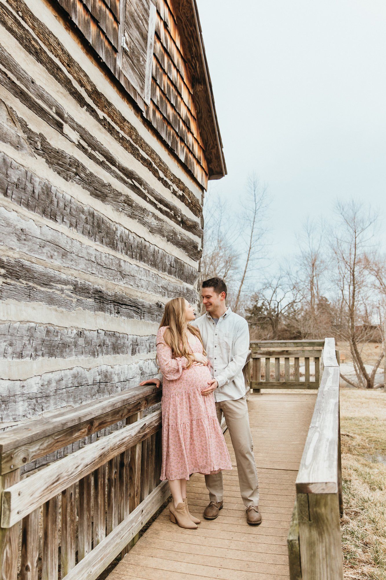 Husband and wife stand at the entrance to a house as wife holds her baby bump