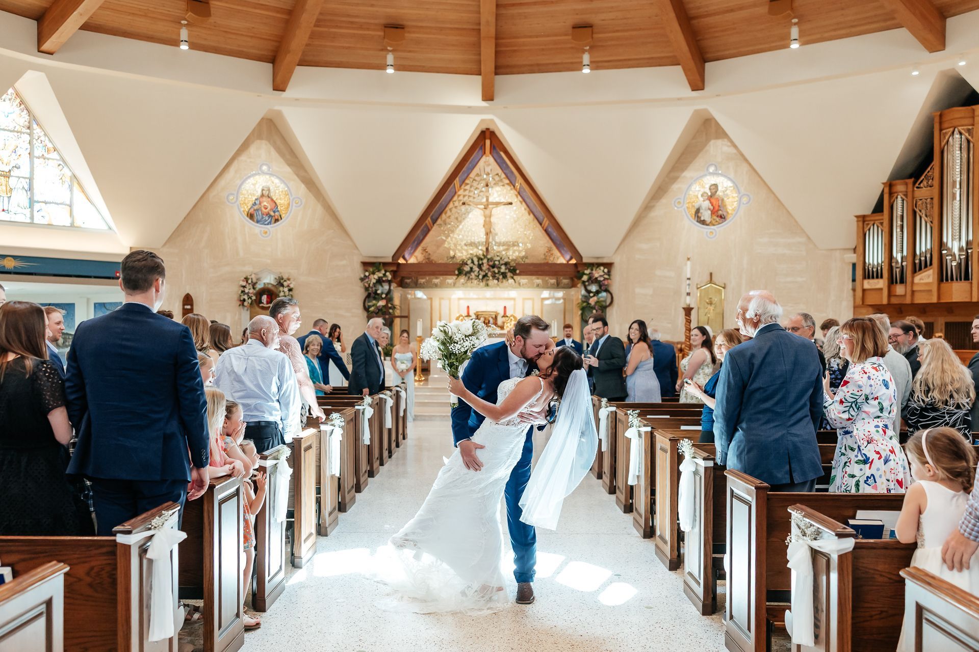 Newly married couple kisses and walks down the aisle, cheered by guests in a church.