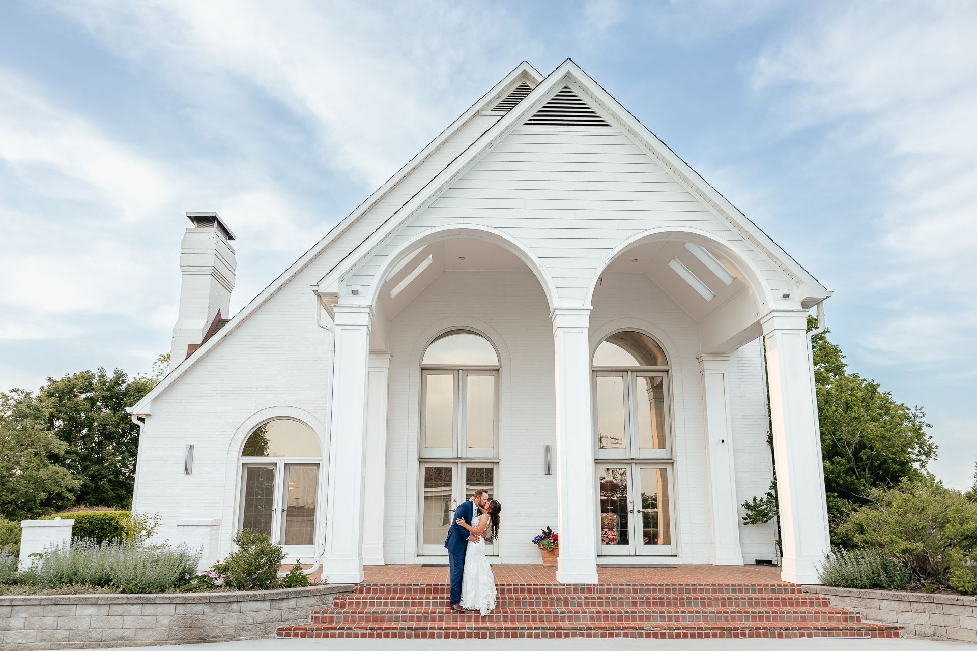 Couple kissing on steps of a white wedding venue with arched entryways and columns.