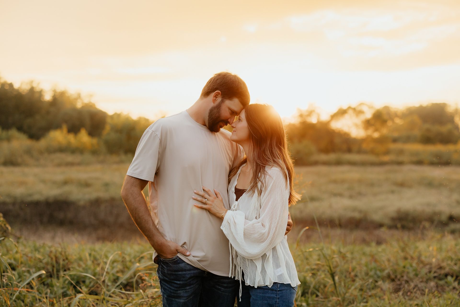 Couple embracing, about to kiss, in field at sunset. Warm golden light.