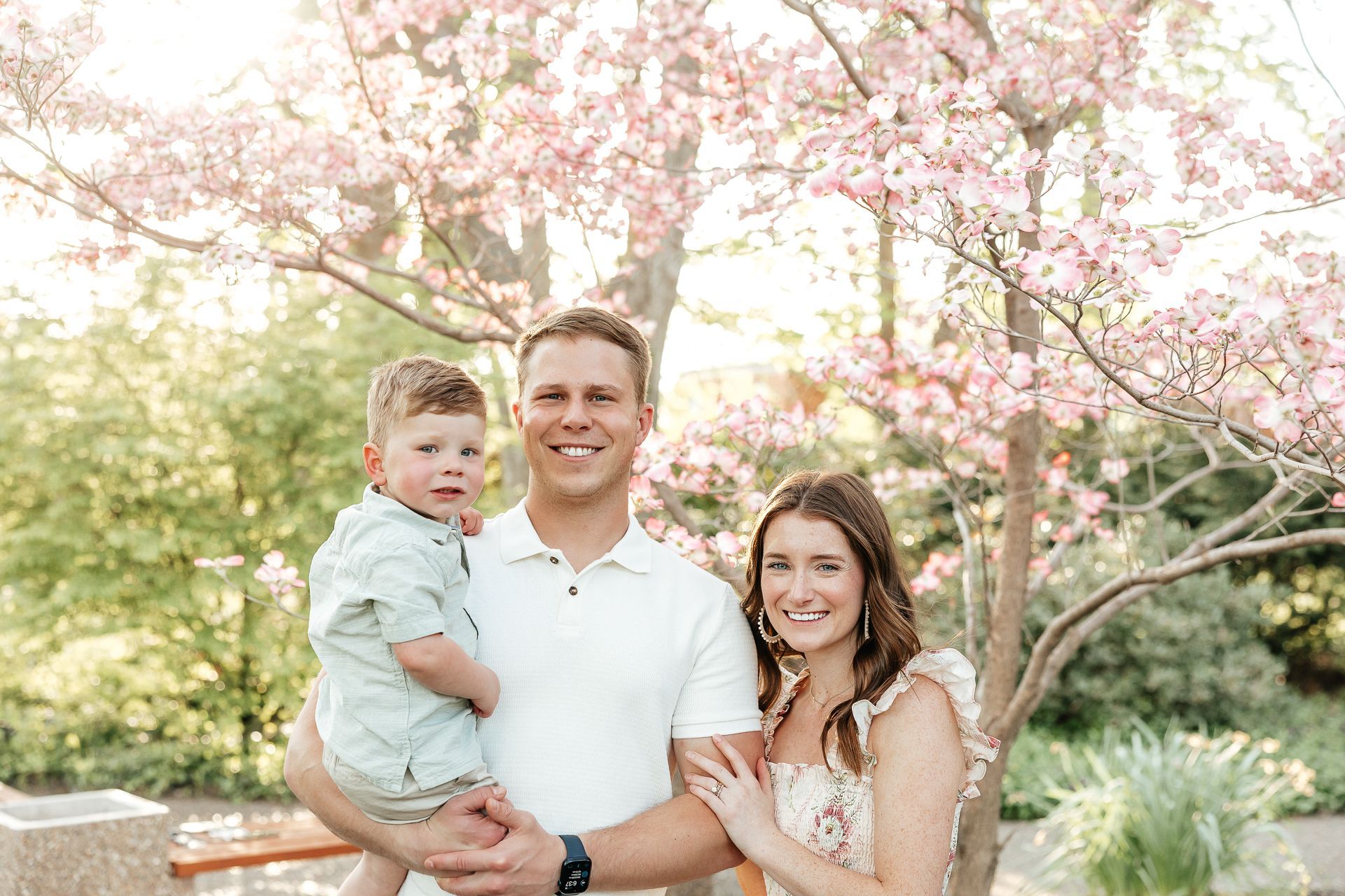 Family of three posing under a blossoming tree, smiling.