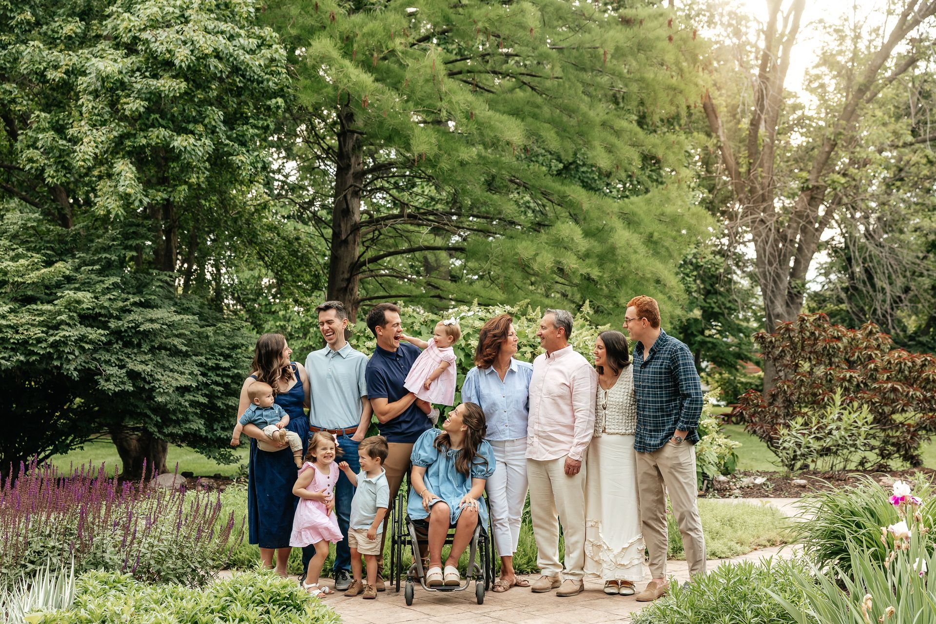Family posing outdoors with a person in a wheelchair. Trees and flowers in the background.
