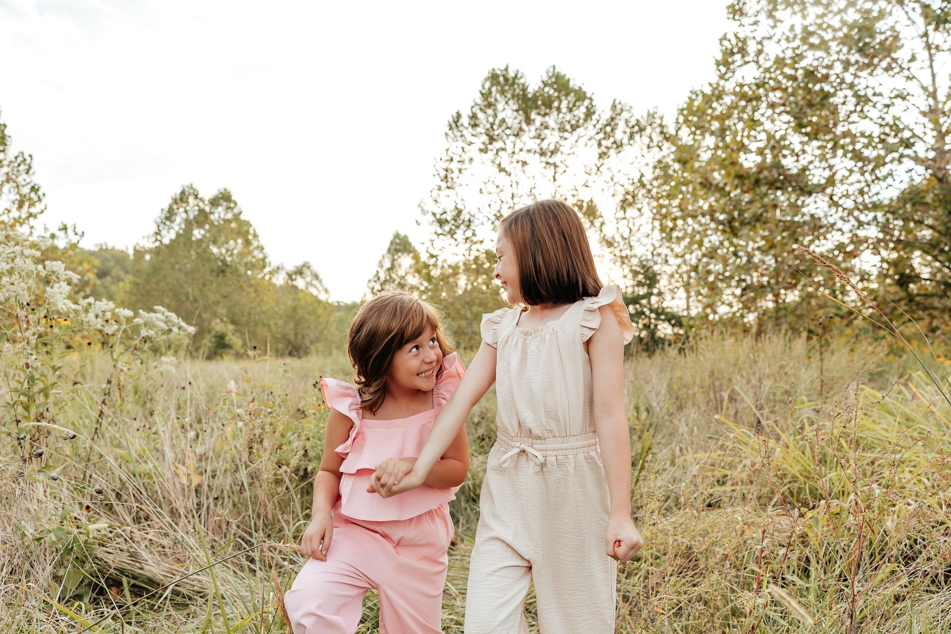 Two girls in matching outfits hold hands in a field, smiling.