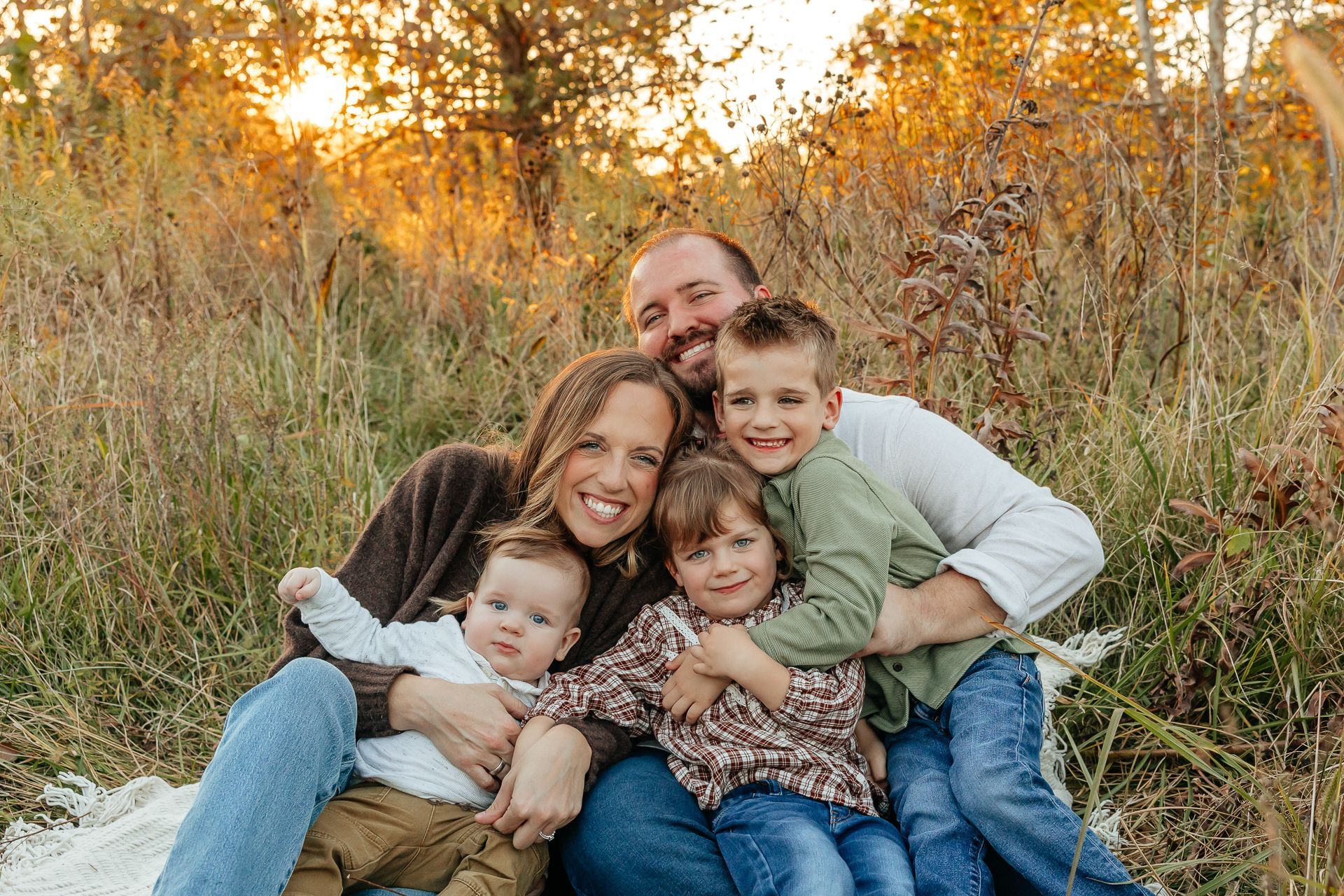 Family of five smiles together outdoors; sunset in background.