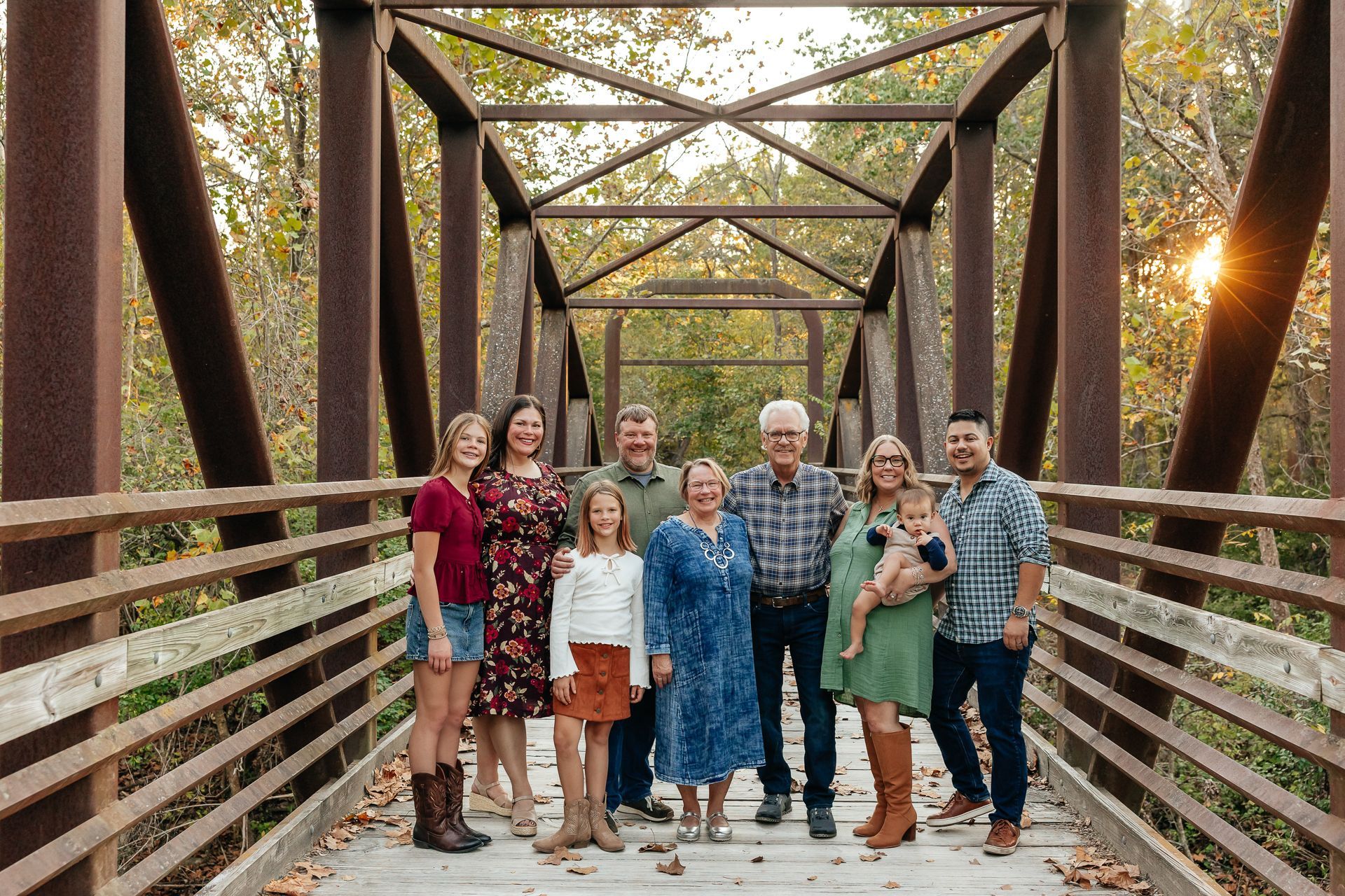 Family posing on a rusty metal bridge in a park. Autumn leaves and trees surround them.
