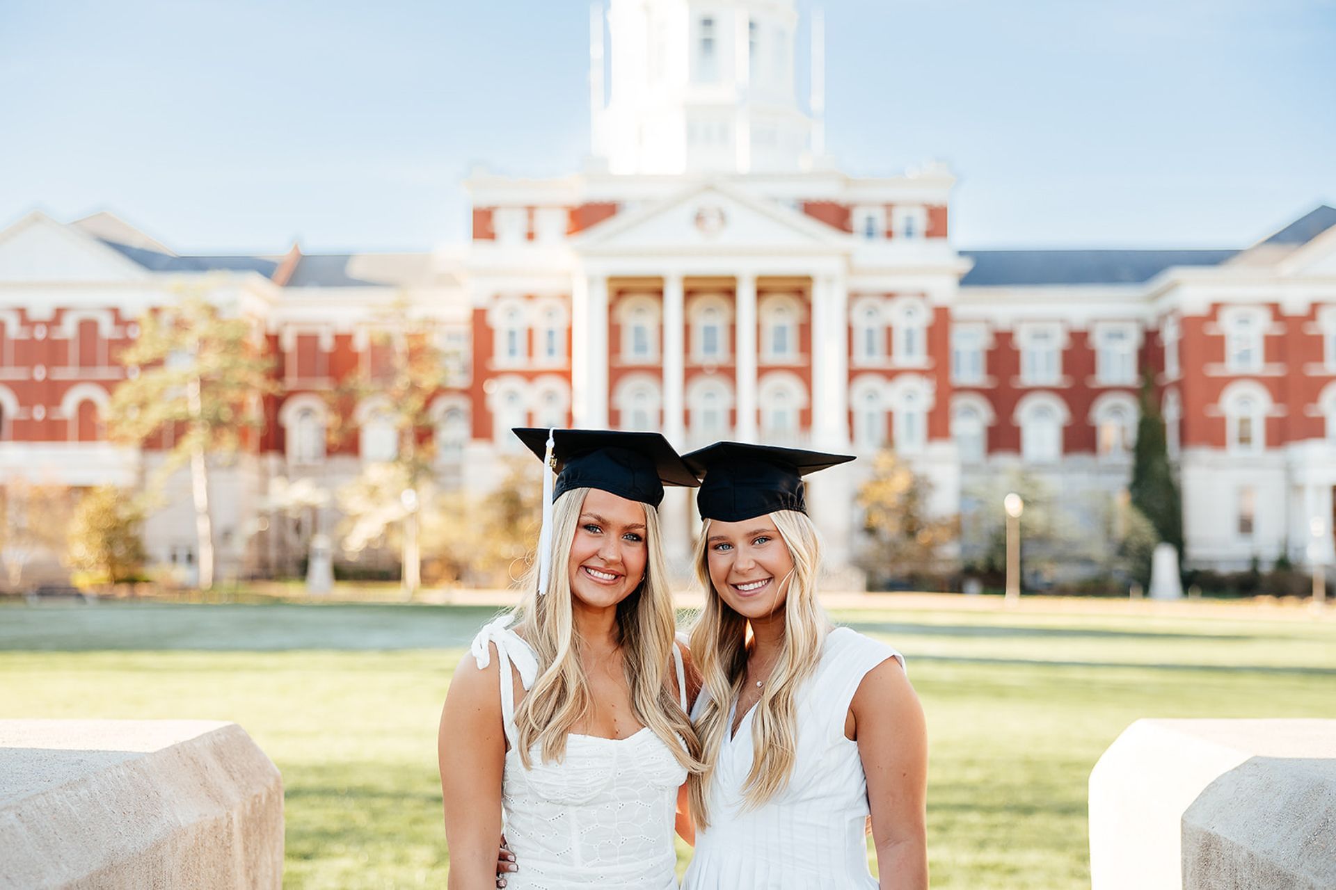 Two graduates in caps and gowns in front of a red brick building with a white dome.