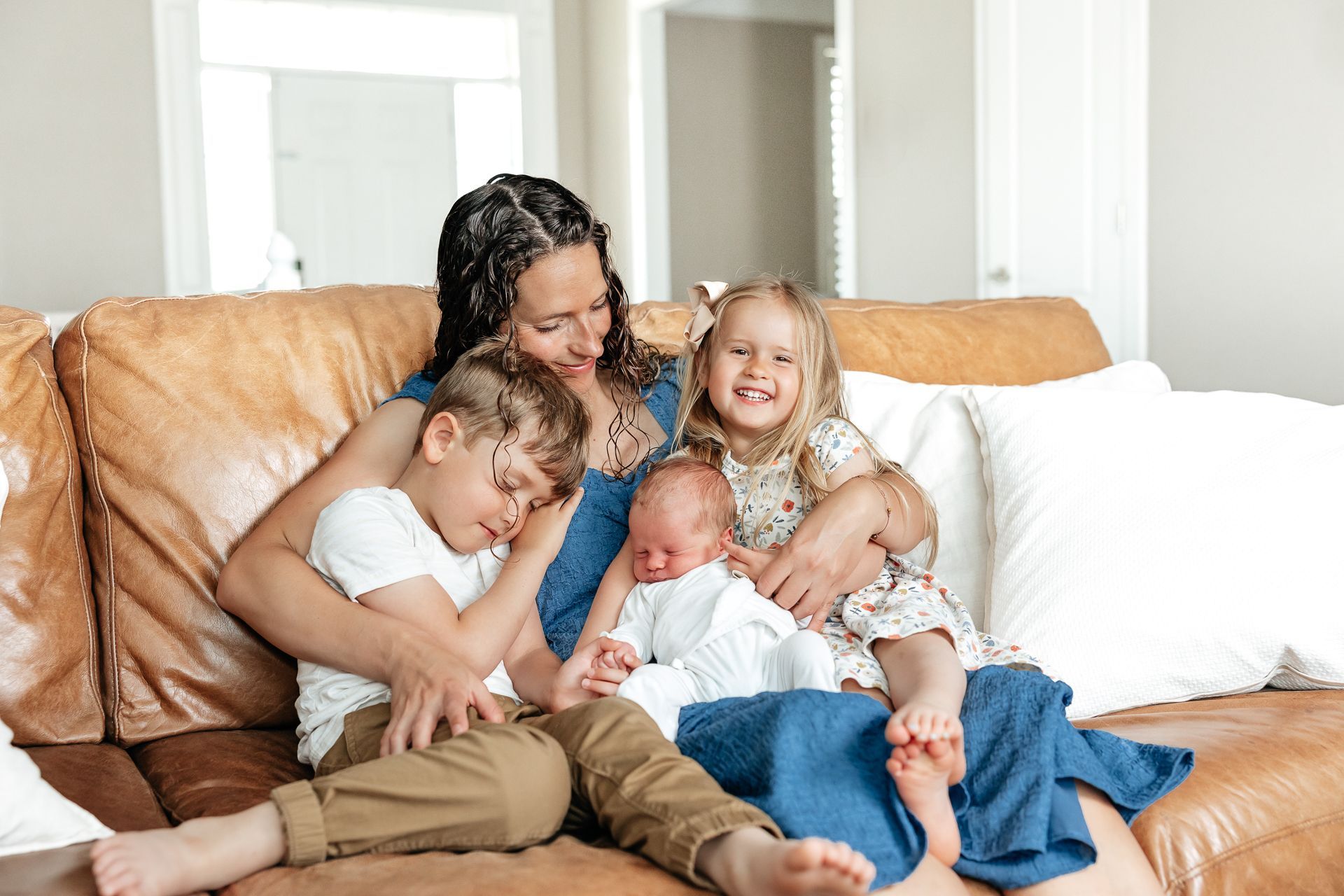 Woman and three children on a brown couch. Youngest child is a newborn.