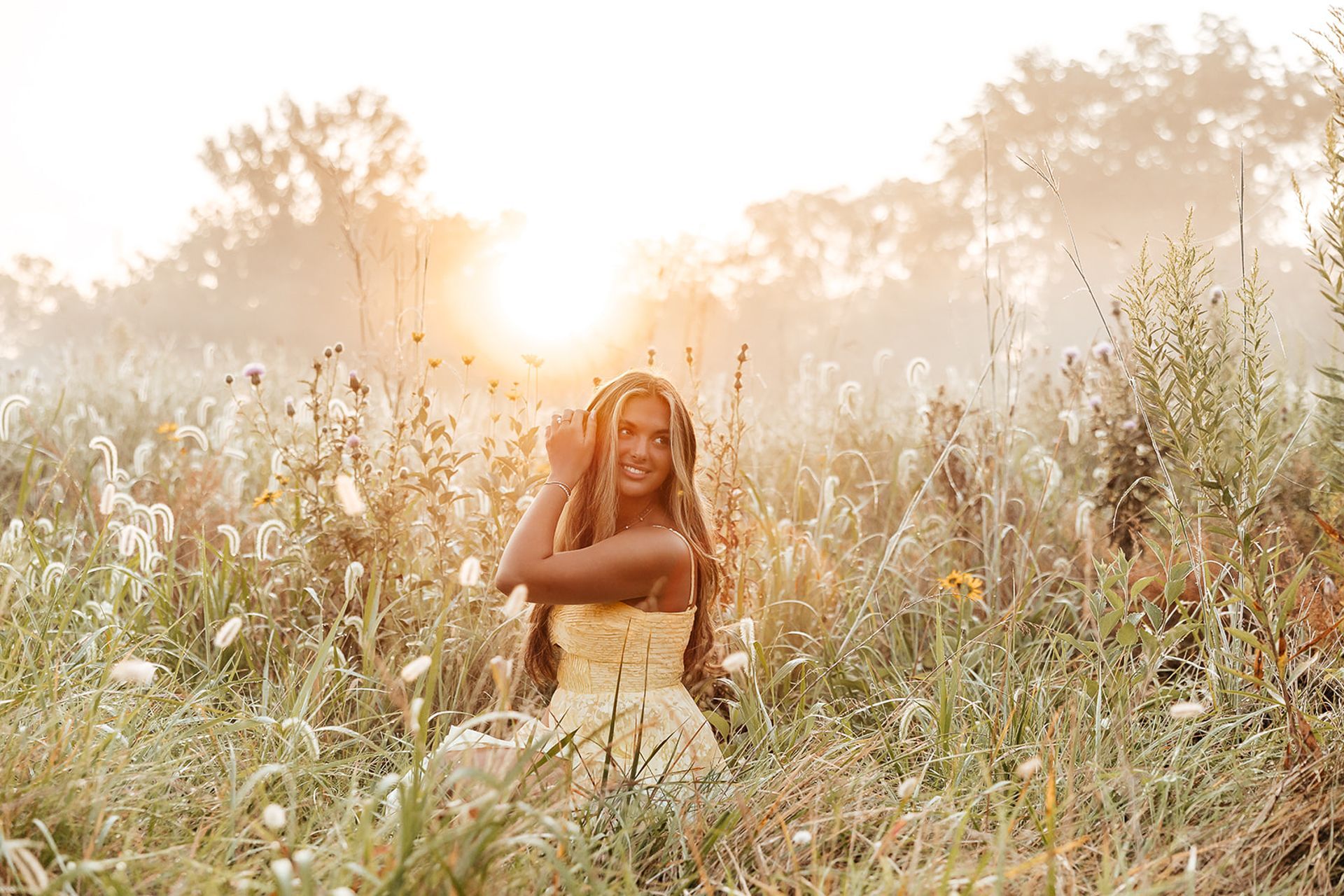 Woman in yellow top sits in tall grass, smiling at the sun.