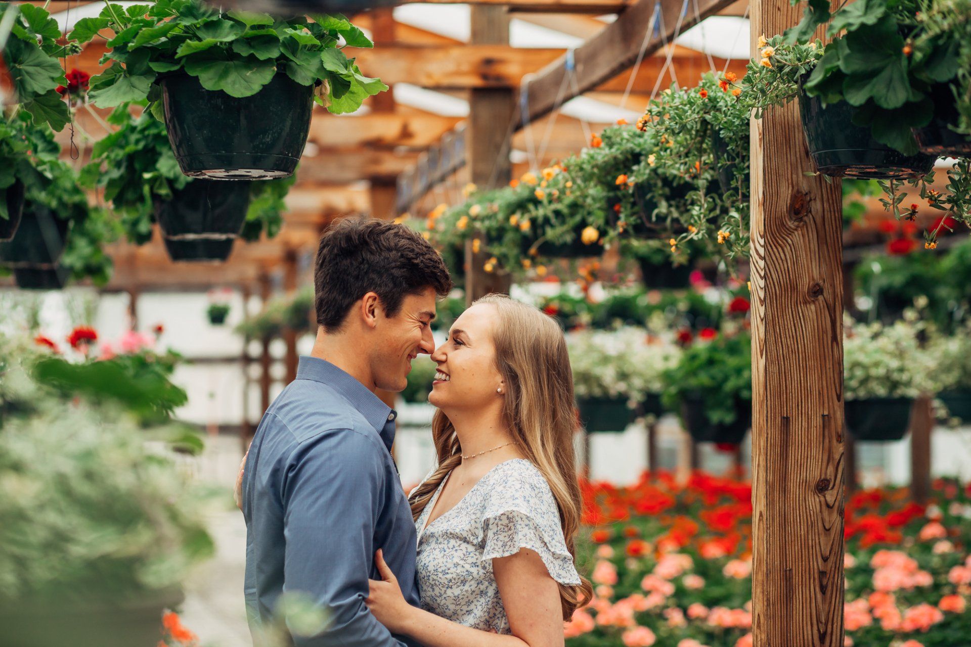 Engaged couple look at each other as they pose in a greenhouse