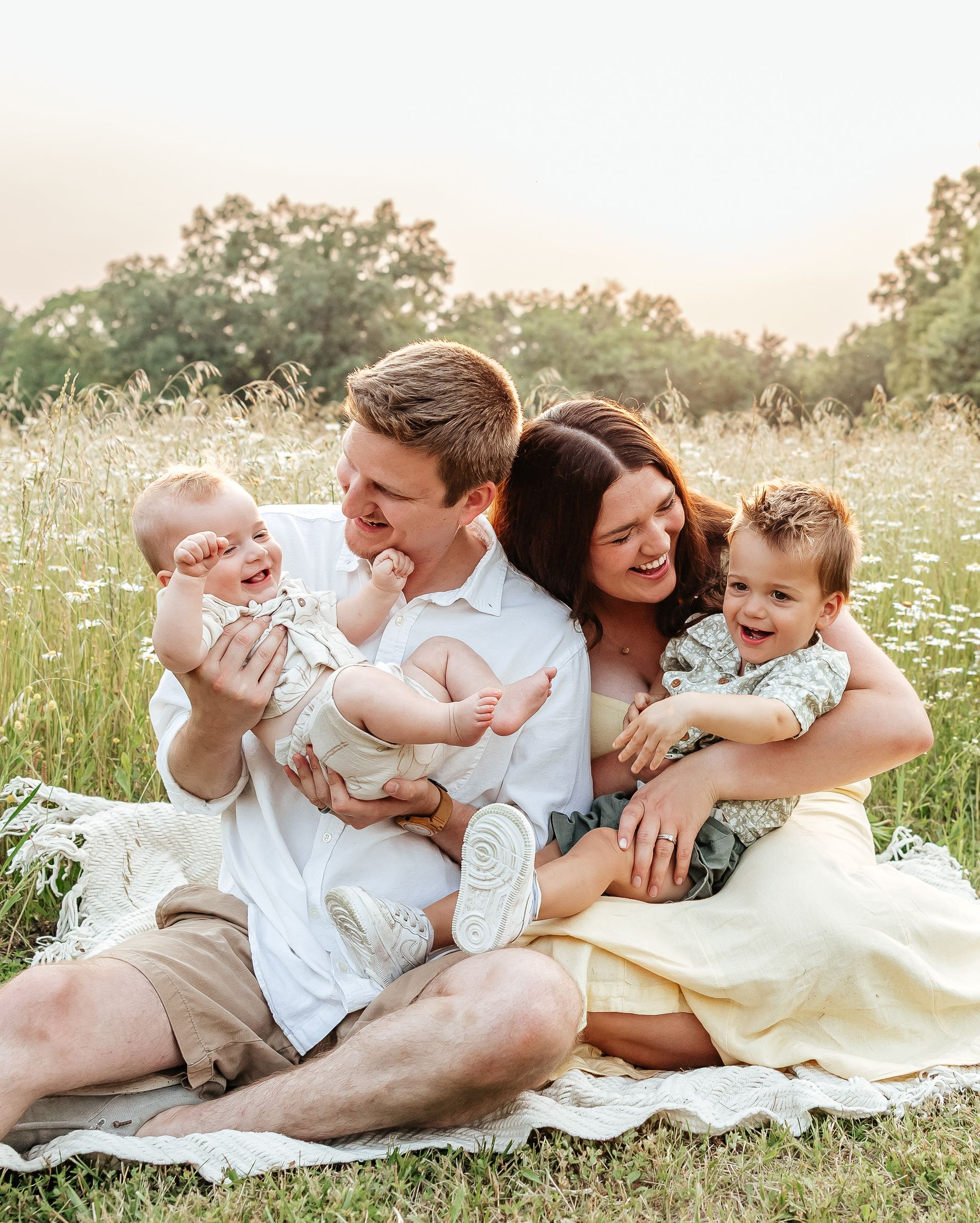 Family of four laughing together in a field of wildflowers.