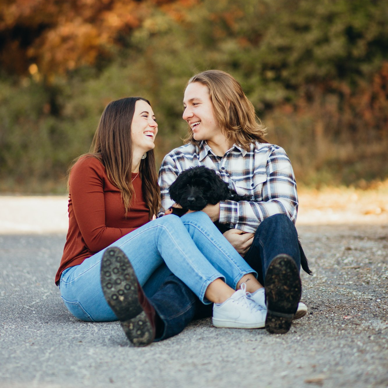 Couple sits on the ground with their dog and looks at each other