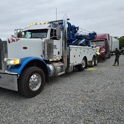 A white and blue tow truck is parked in a gravel lot
