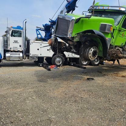 A green semi truck is being towed by a tow truck.