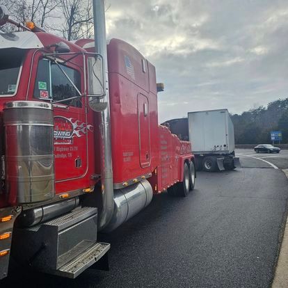 A red tow truck is parked on the side of the road next to a white semi truck.
