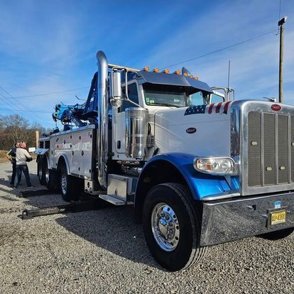 A white and blue tow truck is parked in a gravel lot.