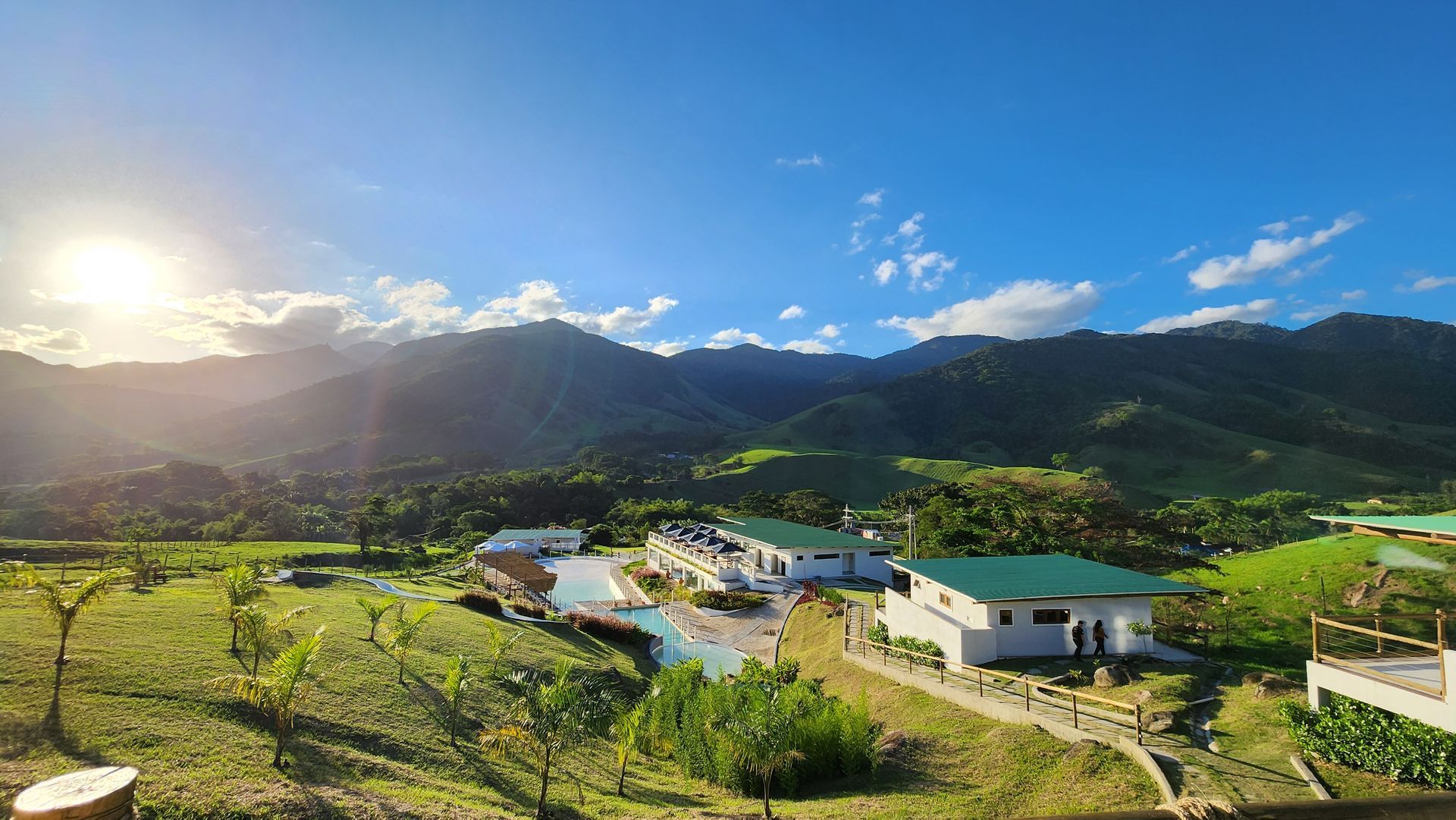Piscina com cascata e assentos dentro da piscina. Prédio branco ao fundo.