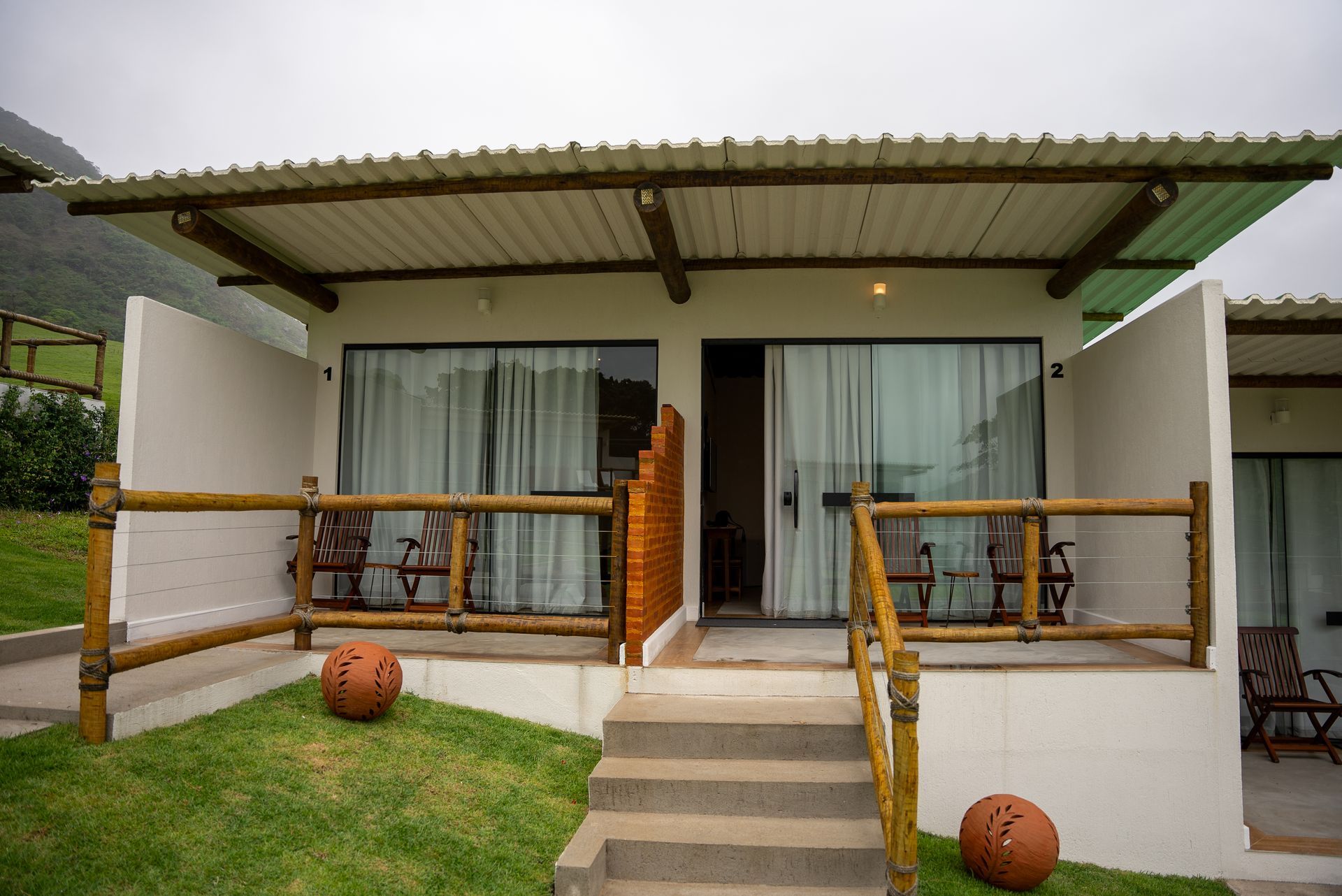 Quartos de hotel brancos com grades de madeira na varanda, cenário de montanhas, céu nublado.