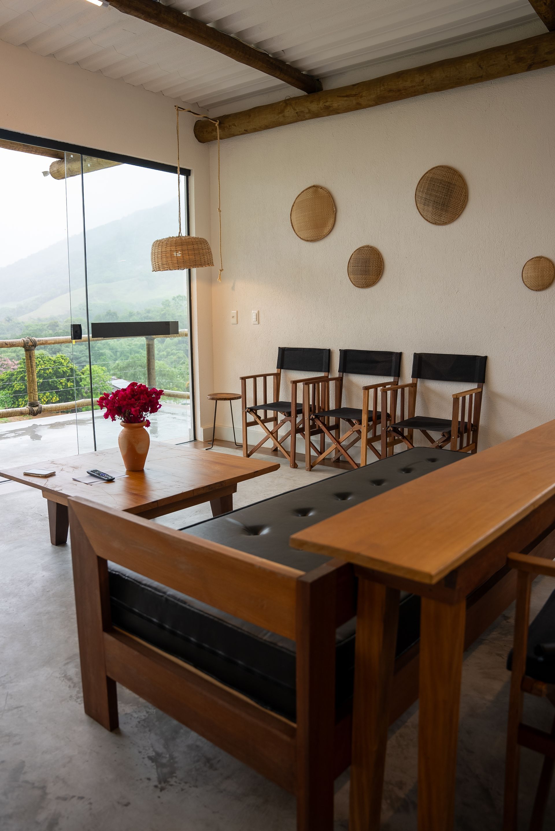 Sala de estar com móveis de madeira, parede de vidro e vista para as montanhas. Paredes bege com círculos decorativos.