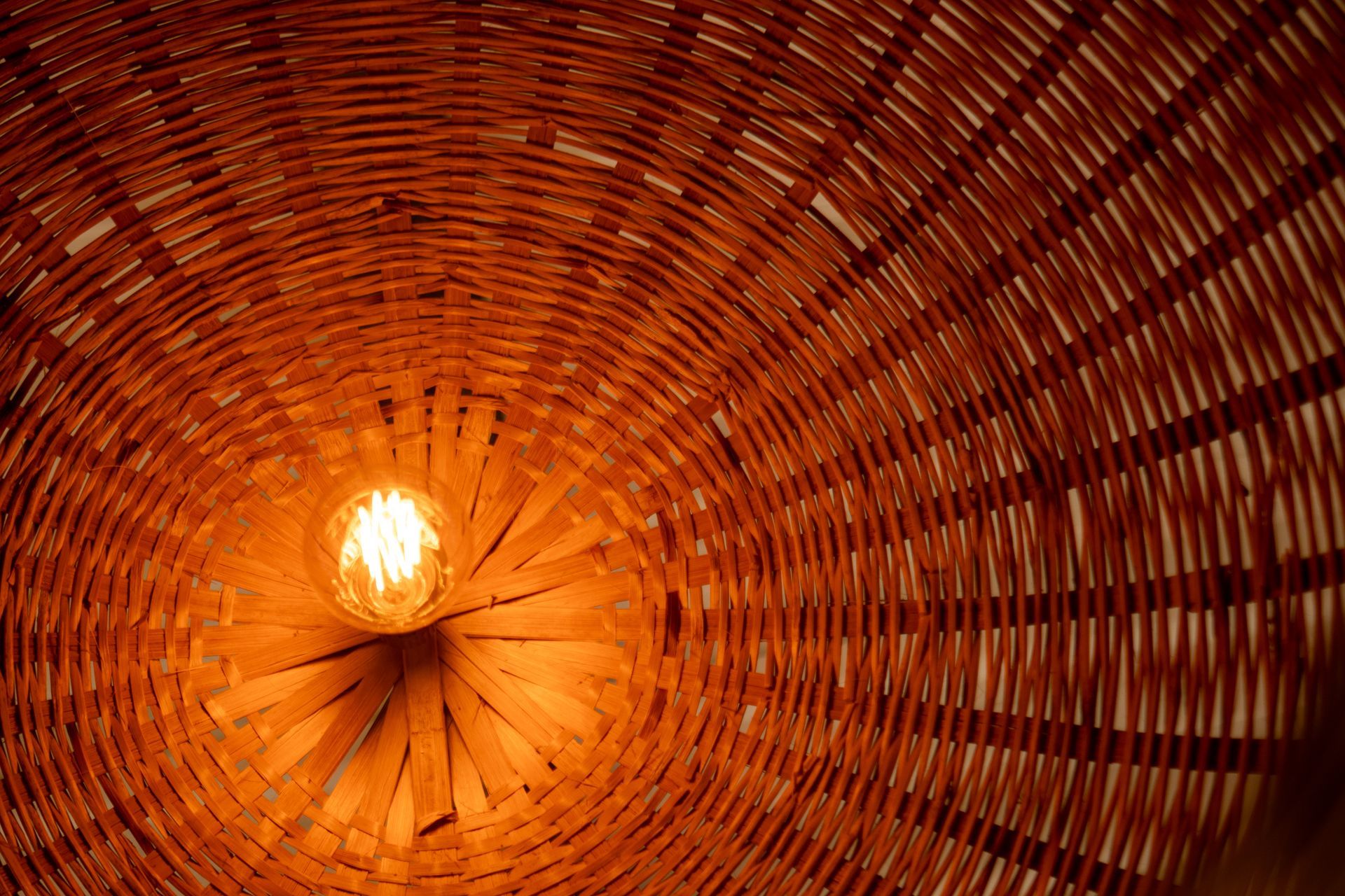 Olhando para um abajur de bambu trançado, com uma lâmpada brilhante no centro.