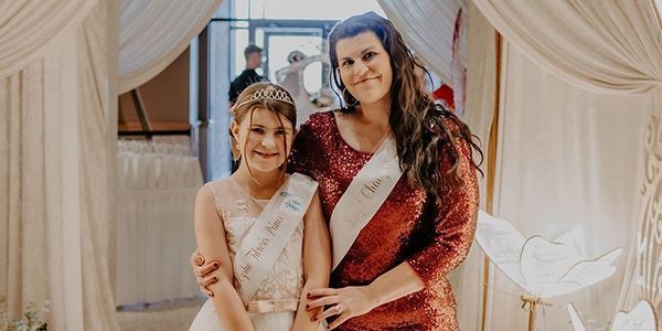 A mom and daughter pose in fancy princess gowns.