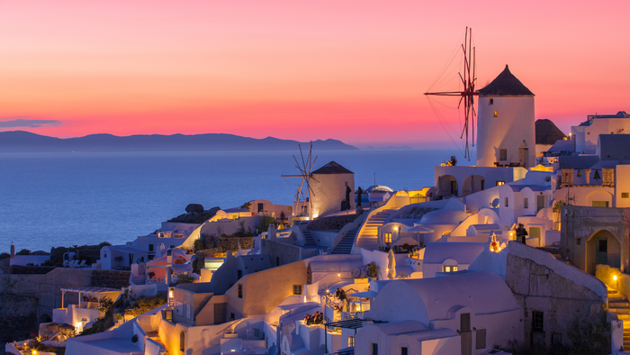 Sunset over Santorini, Greece: white buildings, windmills, and Aegean Sea under a pink and blue sky.
