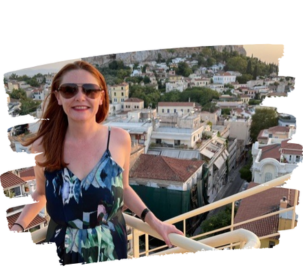 Woman on a rooftop smiles at the camera, with the Acropolis in Athens in the background.