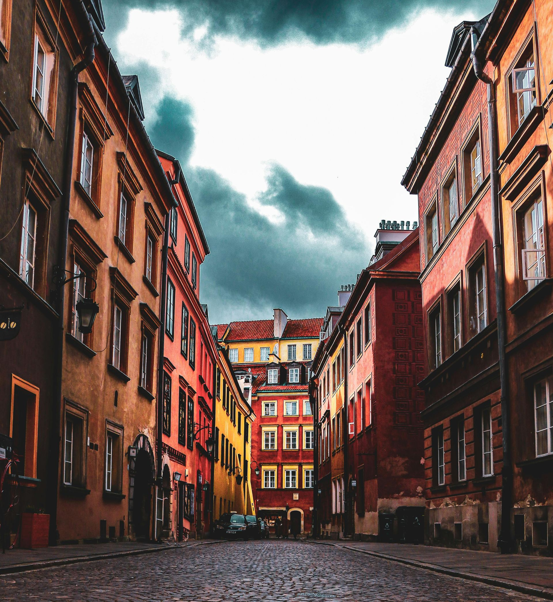 Narrow cobblestone street lined with colorful historic buildings under a cloudy sky.