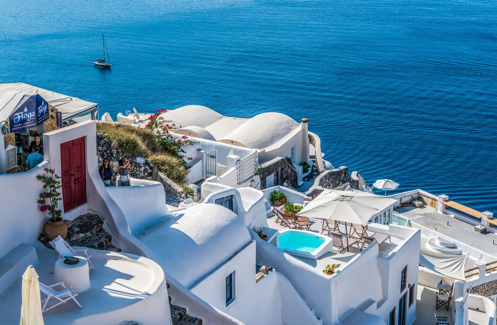 White buildings with blue domes on a cliff overlooking the Aegean Sea.