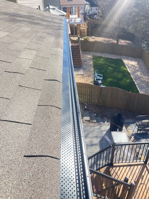 A gutter on the roof of a house with a backyard in the background.
