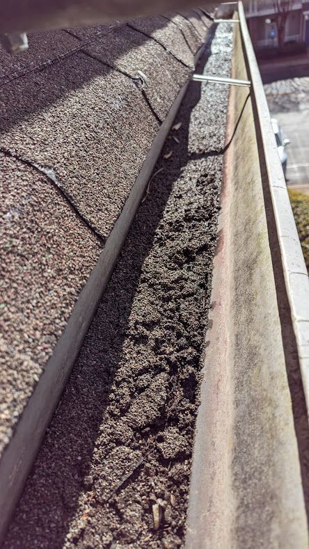 A close up of a gutter on a roof with a lot of dirt on it.