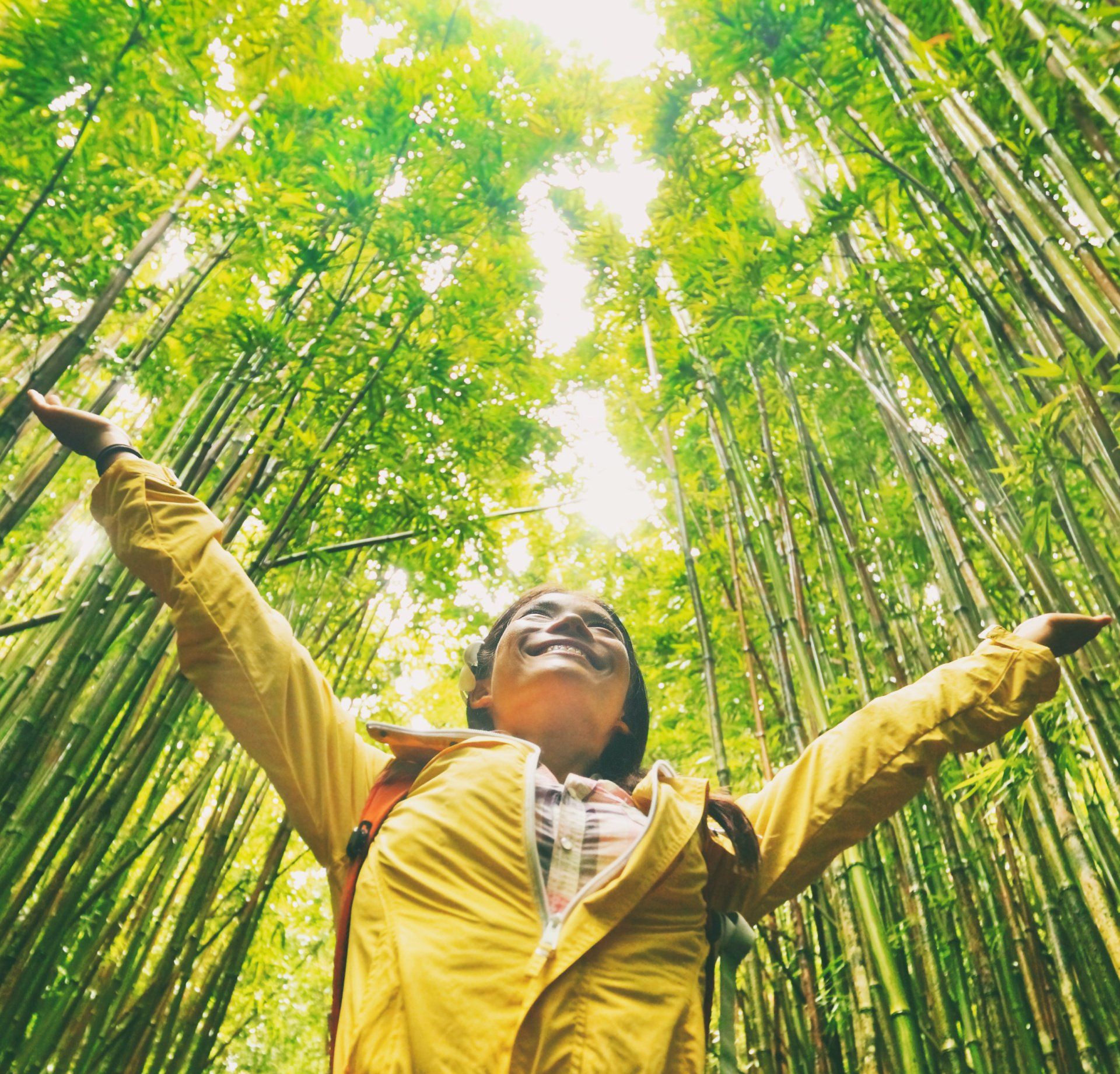 A woman is standing in a bamboo forest with her arms outstretched.