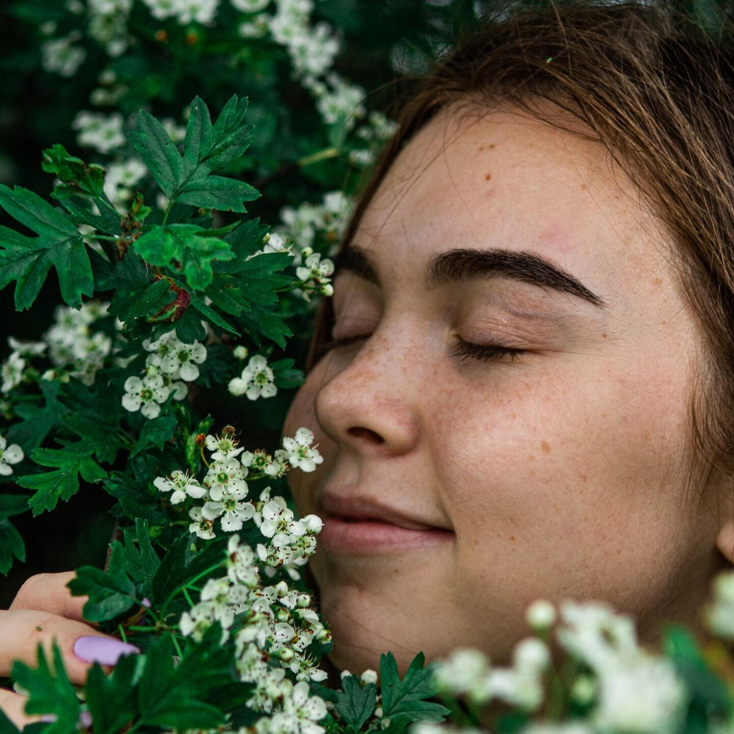 A close up of a woman smelling flowers with her eyes closed.