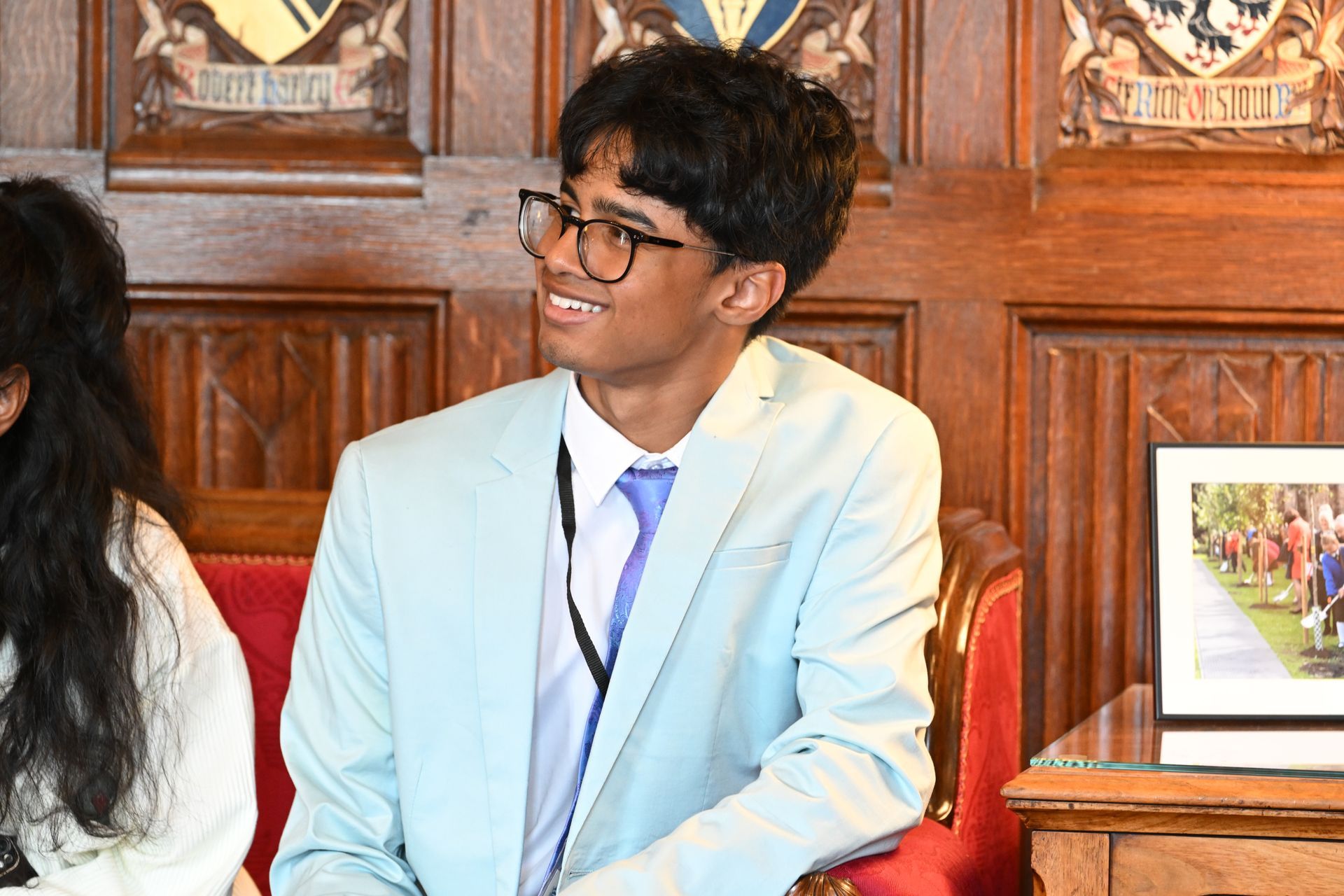 A young man in a suit and tie is sitting in a chair.
