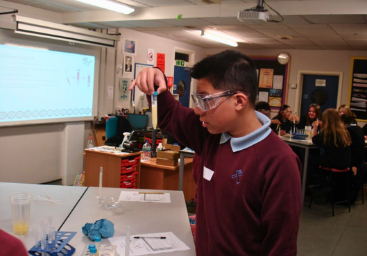 A boy wearing glasses is holding a test tube in a classroom