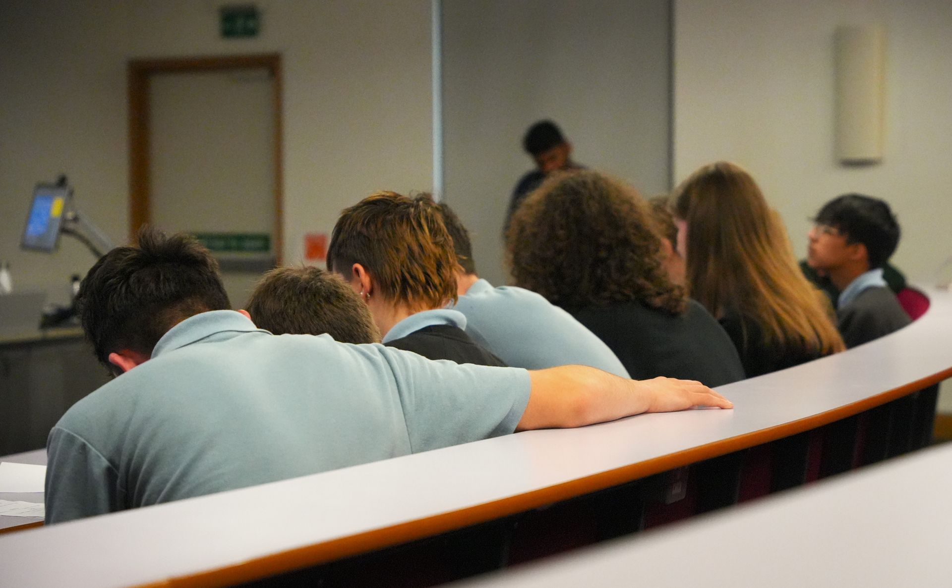 A group of people are sitting in a classroom with their backs to the camera.